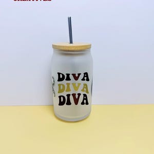 Pode incluir: Copo de vidro fosco com tampa de bambu e canudo prateado. O copo apresenta a palavra "DIVA" em letras pretas, douradas e marrons. No canto superior esquerdo está o texto "JAZZ IT UP CREATIVES" em vermelho e branco.