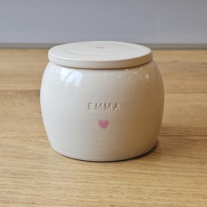May include: White ceramic jar with a lid, featuring the name "EMMA" and a pink heart.