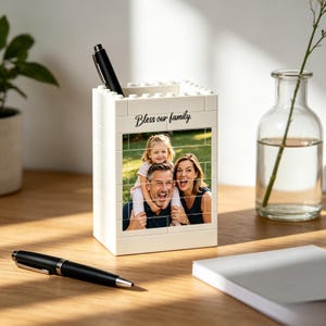 May include: A white rectangular desk organizer constructed from interlocking plastic building blocks. The front features a printed photograph of a family and the text "Bless our family." in black script. A black pen is inserted into the top opening.