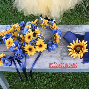 May include: Three sunflower and blue flower wreaths with navy blue ribbons, and a single sunflower with navy blue ribbon. The text "WEDDINGS IN CAMO" is visible on a wooden surface.
