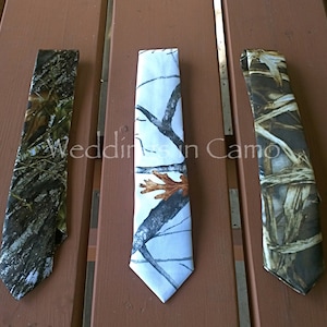 May include: Three different camouflage patterned neckties. The ties are all made of a fabric with a woven texture. The ties are all in a classic necktie shape with a pointed tip. The ties are all in different shades of green, brown, and white.