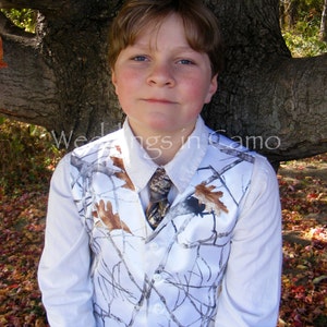May include: A young person wearing a white button-down shirt with a camouflage waistcoat and a brown tie. The waistcoat has a white background with brown branches and leaves.