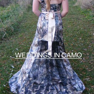 May include: A wedding dress with a camouflage pattern and a large white satin bow. The dress has a one-shoulder design and a lace trim. The text "Weddings in Camo" is visible at the bottom of the image.