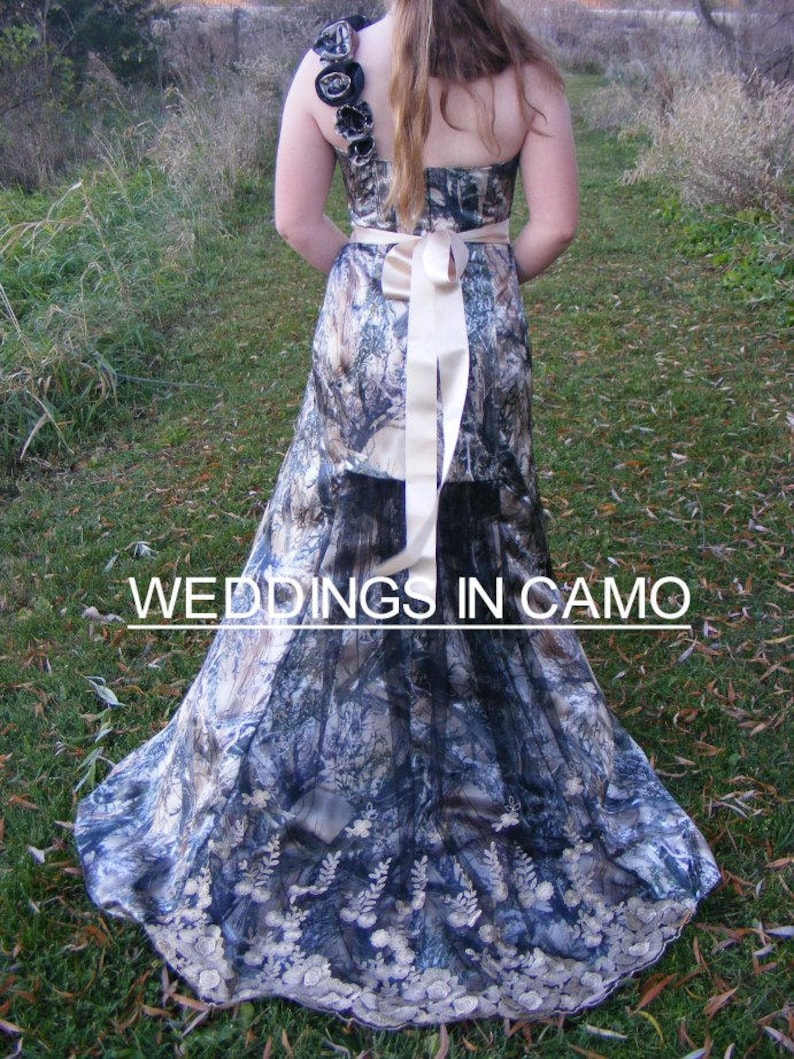 May include: A wedding dress with a camouflage pattern and a large white satin bow. The dress has a one-shoulder design and a lace trim. The text "Weddings in Camo" is visible at the bottom of the image.