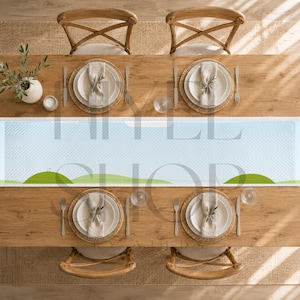 May include: A long rectangular table runner featuring a light blue background with a subtle chevron pattern and a horizontal landscape graphic of green rolling hills. The runner is centered on a wooden dining table with four place settings.