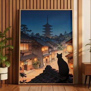 May include: A framed wall art print depicting a black cat sitting on a dark tiled roof overlooking a Japanese village at twilight. The scene features traditional wooden buildings, glowing orange paper lanterns, and a pagoda in the distance.