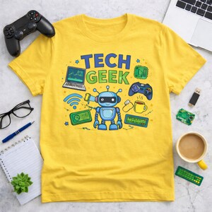 Peut inclure: T-shirt jaune avec l'inscription "TECH GEEK" en bleu et vert, orn&eacute; d'un robot de dessin anim&eacute; et de graphiques li&eacute;s &agrave; la technologie. Le design comprend un ordinateur portable, une manette de jeu et une tasse de caf&eacute;.