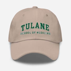May include: A tan baseball cap with the word "TULANE" in green block letters arched across the front, above the words "SCHOOL OF MEDICINE". The cap has a curved brim and a button on top.