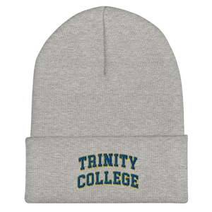 May include: A light gray beanie with the words "TRINITY COLLEGE" embroidered in blue and yellow. The beanie is made of a soft, knitted material and has a folded brim.