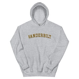 May include: A light gray hooded sweatshirt with the word "VANDERBILT" printed across the chest in a gold-colored, collegiate-style font. The sweatshirt has a drawstring hood and a kangaroo pocket.
