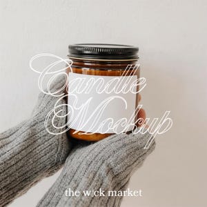 Puede incluir: Un tarro de vidrio marrón con tapa negra y una etiqueta blanca en blanco. El tarro lo sostiene una persona que lleva un suéter gris. El texto "Candle Mockup" está superpuesto en la imagen, junto con "the wick market".