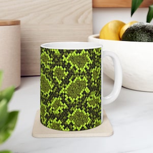 Può includere: Tazza in ceramica bianca con un audace motivo a pelle di serpente verde e nero. La tazza ha un manico standard e poggia su un sottobicchiere beige. Il motivo avvolge l'intera tazza, creando un look audace. Perfetta per caffè o tè.