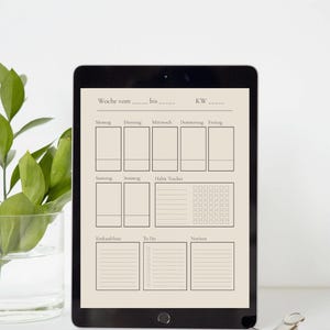 Könnte beinhalten: Ein schwarzes Tablet mit einem Wochenplaner, der Abschnitte für jeden Tag, einen Gewohnheitstracker, eine Einkaufsliste, eine To-Do-Liste und Notizen enthält. Der Text ist auf Deutsch. Eine Pflanze und eine Büroklammer sind im Hintergrund.