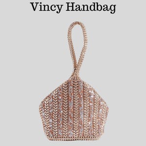 Puede incluir: Un bolso de mano en oro rosa con un diseño geométrico y un asa. El bolso está cubierto de pequeños adornos brillantes. El texto "Vincy Handbag" está en la parte superior.