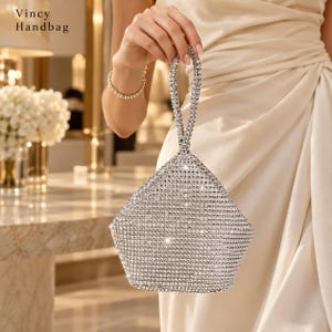 Puede incluir: Un bolso de mano Vincy con una silueta triangular cubierta de brillantes diamantes de imitación plateados. El bolso tiene un asa superior única hecha del mismo material de pedrería, creando una apariencia cohesiva y brillante con una forma geométrica estructurada.