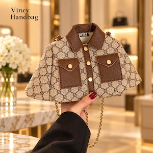 Puede incluir: Un bolso de mano Vincy con forma de chaqueta, estampado de monograma beige y marrón, cuello marrón oscuro, dos bolsillos delanteros y botones dorados. El bolso incluye una correa de cadena dorada y una etiqueta con el texto PORT.