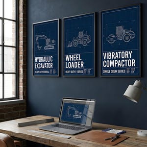 Könnte beinhalten: Drei gerahmte Blaupausen von Baumaschinen: ein Hydraulikbagger, ein Radlader und ein Vibrationsverdichter. Die Drucke werden an einer dunkelblauen Wand über einem Holzschreibtisch mit einem Laptop angezeigt.