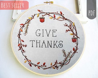 May include: Embroidered hoop art with a fall-themed wreath of brown branches, red berries, and orange leaves surrounding the text "GIVE THANKS".