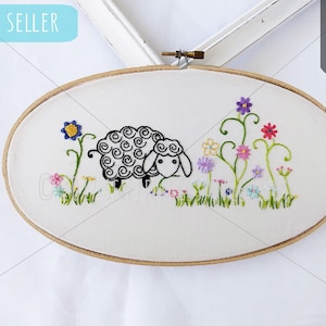 May include: Embroidered hoop art featuring a black and white sheep with curly wool, surrounded by colorful flowers and green leaves. The hoop is oval shaped and has a wooden frame.