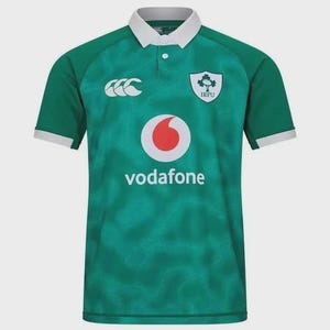 Könnte beinhalten: Grünes Rugby-Trikot mit weißem Kragen und Manschetten. Es zeigt das IRFU-Logo, ein Vodafone-Logo und ein Canterbury-Logo. Das Trikot hat ein strukturiertes Muster und einen Knopfkragen.