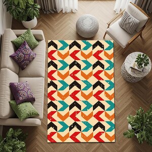 Op de afbeelding: Rechthoekig vloerkleed met een geometrisch patroon van rode, zwarte, turquoise en oranje pijlen op een crèmekleurige achtergrond. Het vloerkleed heeft een distressed, vintage uitstraling en ligt op een houten vloer. Het vloerkleed is omringd door meubels.