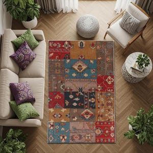 Op de afbeelding: Een bovenaanzicht van een woonkamer met een kleurrijk patchwork vloerkleed. Het kleed heeft patronen in rood, blauw, goud en bruin. Een beige bank met groene en paarse kussens staat links. Een witte stoel en bijzettafel staan rechts.