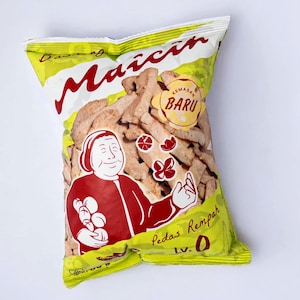 Peut inclure: Un sachet de snacks jaune avec le nom de marque Maicih en écriture rouge, une illustration rouge d'une personne, et le texte KEMASAN BARU, Pedas Rempah, et Lv. 0. Le sachet montre des morceaux de snacks croustillants brun clair.