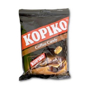 Op de afbeelding: Een zwart en oranje plastic zakje met Kopiko koffiesnoepjes. De verpakking bevat de witte tekst KOPIKO, de woorden Coffee Candy en een afbeelding van een koffieboon boven een donkerbruin snoepje. Het nettogewicht is 150 gram.