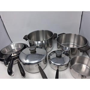 May include: A collection of stainless steel cookware including various pots and pans with black handles and lids. The set features multiple sizes of saucepans, a large stockpot, and a shallow skillet, all with a polished metallic finish.