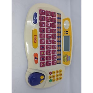 May include: A cream-colored VTech Phonics Reading Center electronic learning toy featuring a QWERTY-style keyboard with pink letter keys, a yellow help button, a blue mouse, a small LCD screen, a speaker, and a yellow numeric keypad on the right.