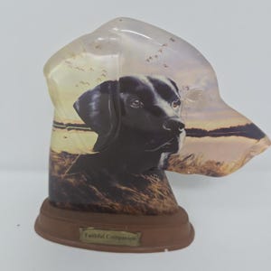 May include: A decorative dog figurine with a black and white dog portrait, set against a sunset scene with flying birds. The base is brown, and the text "Faithful Companion" is displayed on the front.