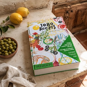 May include: A hardback cookbook titled 1080 Recipes by Simone and Ines Ortega, published by Phaidon. The white cover features colourful hand-drawn illustrations of food, including a rooster, mushrooms, and citrus, with a green corner text block.