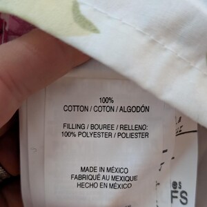 May include: Close-up of a fabric label with text indicating 100% cotton and polyester filling. The label also states "Made in Mexico" in English, French, and Spanish. The fabric has a floral pattern.