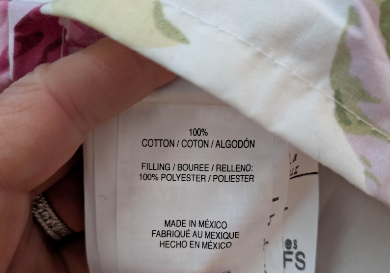 May include: Close-up of a fabric label with text indicating 100% cotton and polyester filling. The label also states "Made in Mexico" in English, French, and Spanish. The fabric has a floral pattern.