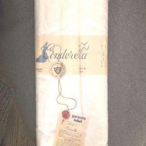 Pode incluir: Um pacote retangular embrulhado em plástico transparente. O pacote apresenta um rótulo com a palavra "Cinderella" em escrita cursiva, uma silhueta de mulher e uma etiqueta "garantie label".