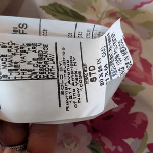 May include: A white tag with black text, including the words "CERTIFICATION" and "FINAL SIZE STD 20 X 26 IN". The tag is partially covering a floral fabric with pink and green flowers.