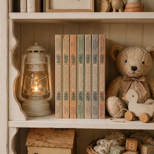 Könnte beinhalten: Ein weißes Holzregal mit sechs Dandelion Library Büchern, einer weißen Metalllaterne mit brennender Kerze, einem beigen Teddybären mit Vichy-Schleife, einer hölzernen Nachzieh-Ente, einem Holzhaus und einem Weidenkorb mit Buchstabenwürfeln.