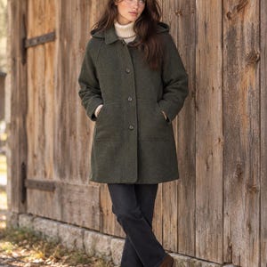 May include: A dark olive green hooded coat featuring a button-front closure, long sleeves, and two front patch pockets. The coat is worn over a cream-coloured turtleneck sweater and dark grey trousers, paired with brown leather ankle boots.