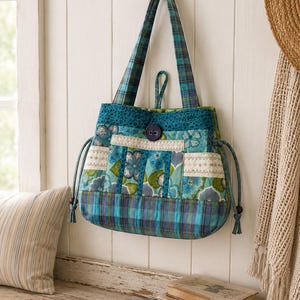 Peut inclure: Un sac fourre-tout matelassé au design patchwork dans des tons bleu sarcelle, bleu et vert. Le sac comprend une base à carreaux, des panneaux à motifs floraux, une fermeture centrale à bouton violet foncé et deux anses à carreaux assorties.
