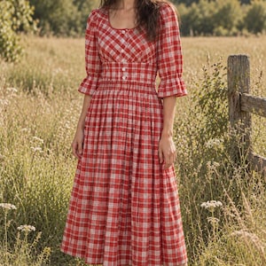 May include: A midi-length dress featuring a red and white plaid pattern, a square neckline, and three-quarter length sleeves with ruffled cuffs. The bodice includes a row of white buttons down the front, a fitted waist, and a gathered, full skirt.