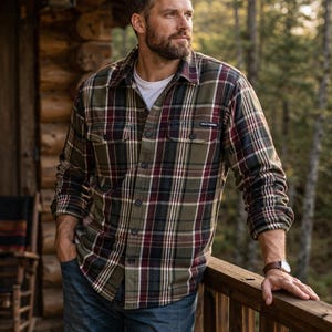 May include: A green, burgundy, and black plaid flannel shirt with a button-down front and two chest pockets. The shirt is worn over a white t-shirt and paired with blue jeans. The Helly Hansen logo is visible on the chest pocket.