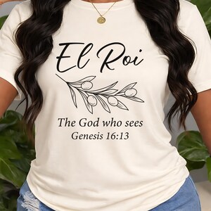 May include: A cream-coloured t-shirt featuring the words "El Roi" and a sprig of olives. Beneath, the text reads "The God who sees Genesis 16:13". A simple, everyday top.