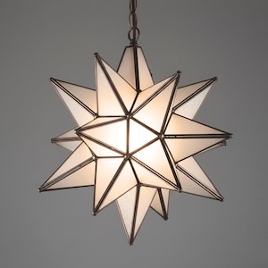 Puede incluir: Una lámpara colgante en forma de estrella con acabado bronce. La lámpara presenta múltiples puntas, con paneles de vidrio esmerilado y un brillo cálido. La luz cuelga de una cadena, creando un elemento de iluminación decorativo y funcional.