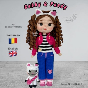 Puede incluir: Una muñeca de ganchillo llamada Gabby & Pandy con pelo rizado castaño, diadema de orejas de gato blanca, bolero rosa, camiseta a rayas negras y blancas y pantalones azules. Una pequeña figura de gato blanco y gris está al lado. Texto: PDF CROCHET PATTERN, Romanian, English, Aprox. 32 cm (12.6 in).