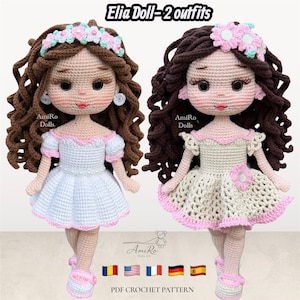 Puede incluir: Dos muñecas de ganchillo con cabello castaño rizado, ojos oscuros y labios rosados. La muñeca izquierda viste un vestido blanco con ribete rosa y diadema floral. La derecha viste un vestido beige con detalles rosas y adorno floral. Texto Elia Doll-2 outfits.