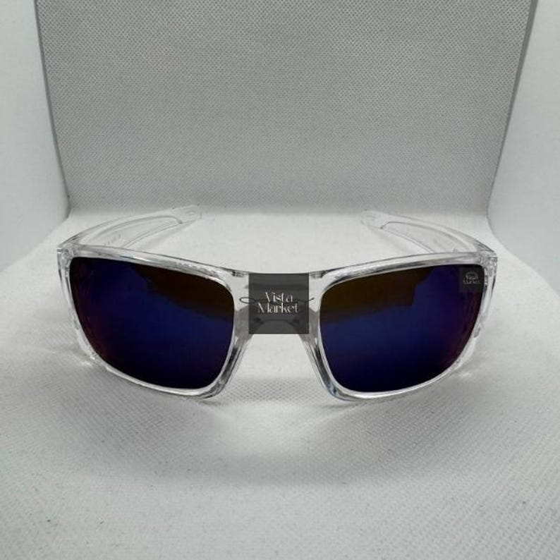 May include: Clear-framed sunglasses with blue-tinted lenses. The sunglasses have a rectangular shape and a clear bridge. The text "Vista Market" is printed on the bridge.
