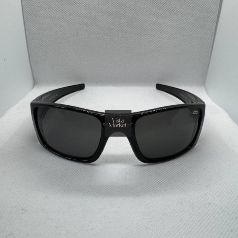 May include: Black rectangular sunglasses with dark lenses. The sunglasses have a thick frame and a bridge with the text "Vista Market". The lenses are dark and appear to be polarized.