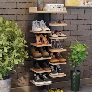 May include: A multi-tiered shoe rack displays various footwear styles. The rack features light-colored wooden shelves and a dark metal frame. Shoes include sneakers, boots, sandals, and slippers in various colors and designs. A decorative vase and books are on top.