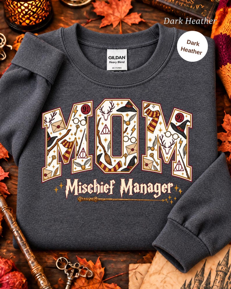 Op de afbeelding: Een donkergrijs gem&ecirc;leerd sweatshirt met ronde hals en het woord MOM in grote letters gevuld met magische iconen zoals toverstokken, hoeden en brillen. Onder het woord MOM staat de tekst Mischief Manager met een toverstokafbeelding.
