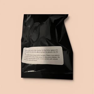 K&ouml;nnte beinhalten: Eine schwarze, gefaltete Plastikt&uuml;te mit einem wei&szlig;en Etikett mit Anweisungen. Der Text auf dem Etikett enth&auml;lt Gebrauchsanweisungen, wie z. B. das Ersetzen des Deckels und das Aufh&auml;ngen der Flasche. Der Hintergrund ist hellbeige.